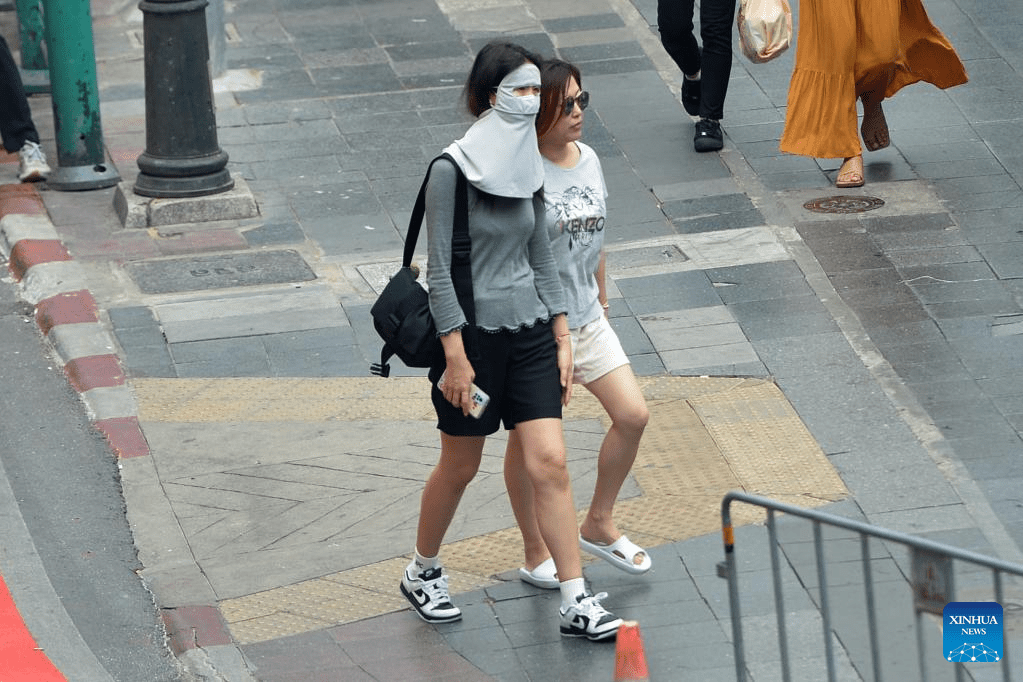A pedestrian shades herself from sunshine with a face mask in Bangkok, Thailand, April 19, 2023. Thailand is experiencing continuous high temperatures recently, with the highest temperature in many provinces exceeding 40 degrees Celsius.