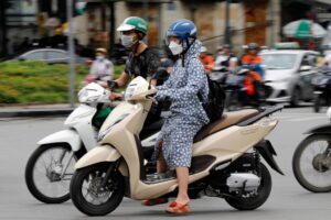 A woman wears long clothing to protect herself from the heat while riding a motorcycle along a street in Hanoi, Vietnam 08 May 2023