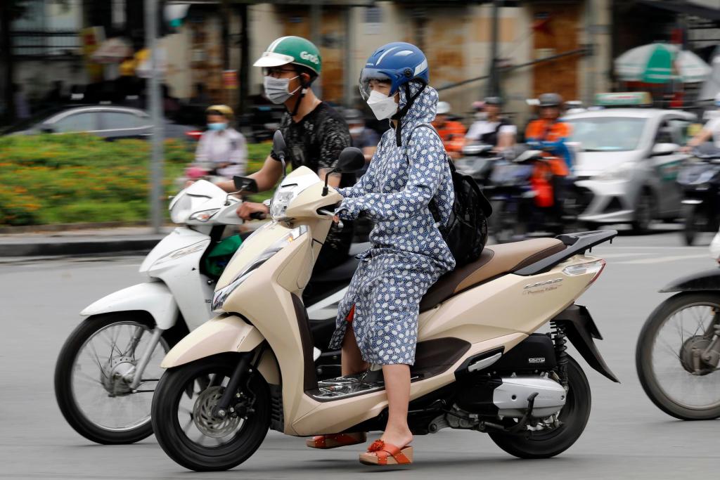 A woman wears long clothing to protect herself from the heat while riding a motorcycle along a street in Hanoi, Vietnam 08 May 2023